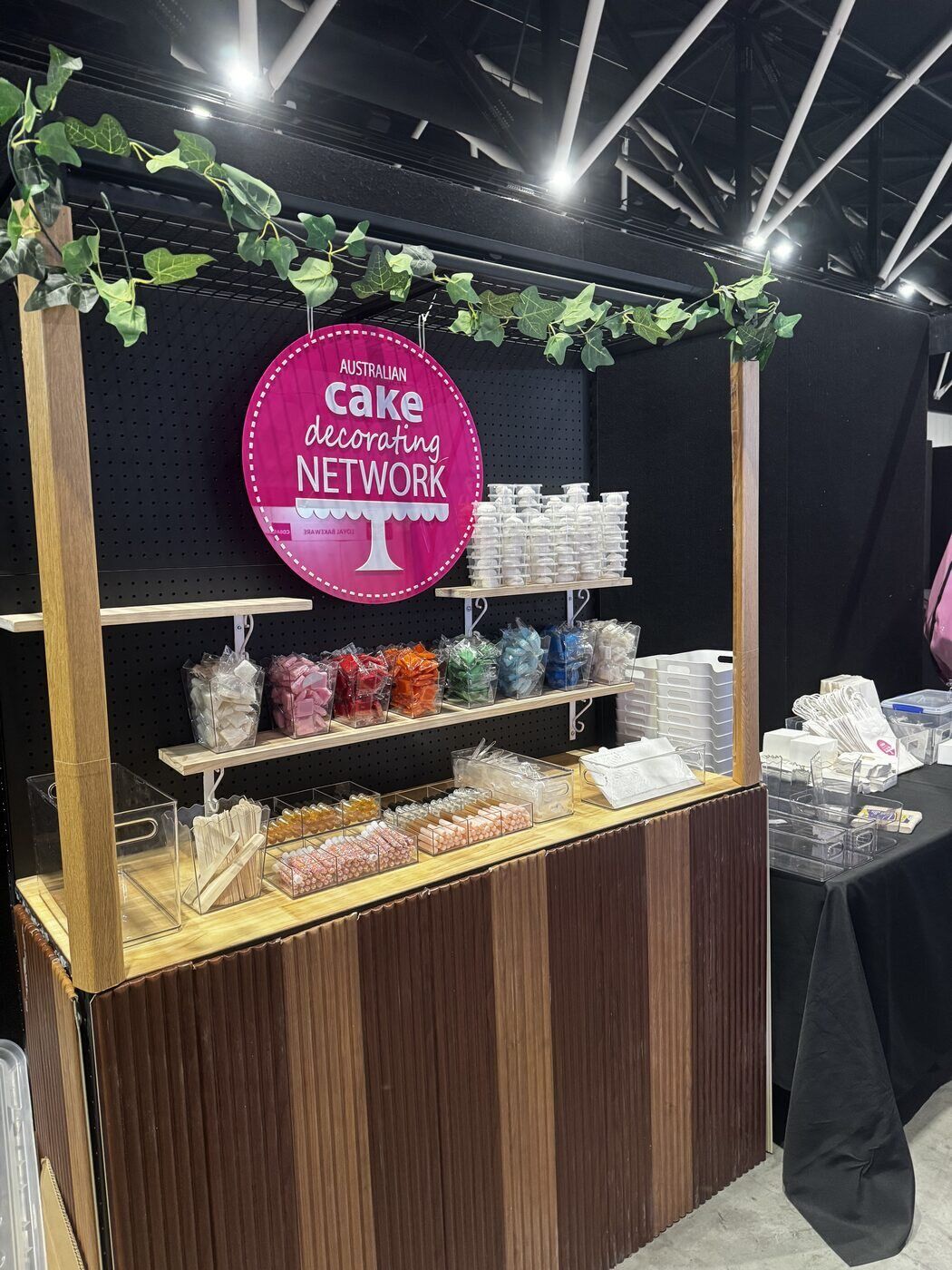 The Cake! Network stand, shelves of sprinkles and decorating supplies under the pink roundel