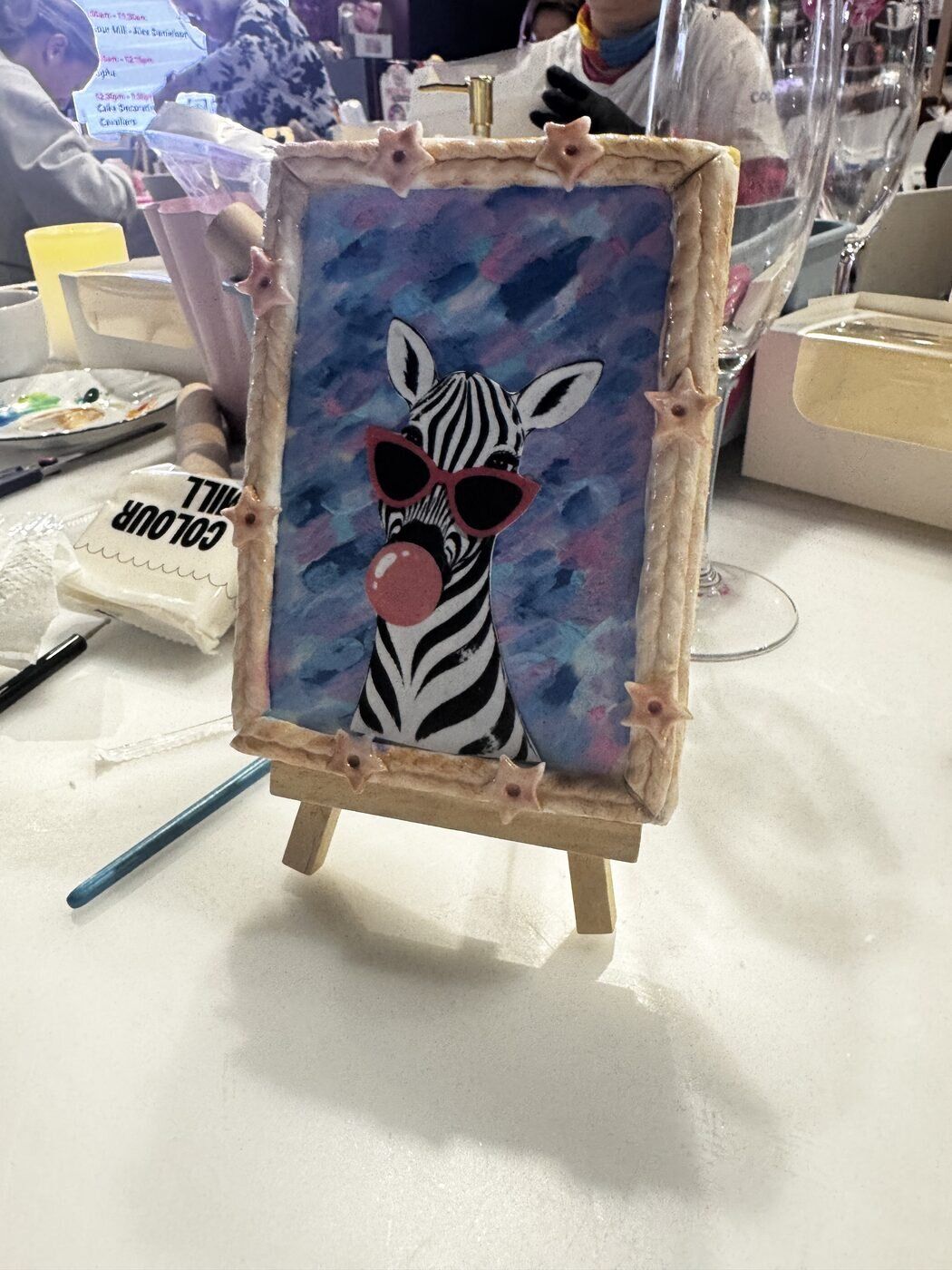 A hand-painted zebra cookie displayed on a small easel