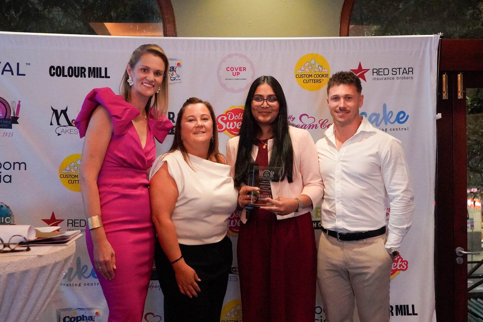 Four guests in front of the sponsor banner, one holding a glass award trophy, at the 2025 ACDN Awards Night
