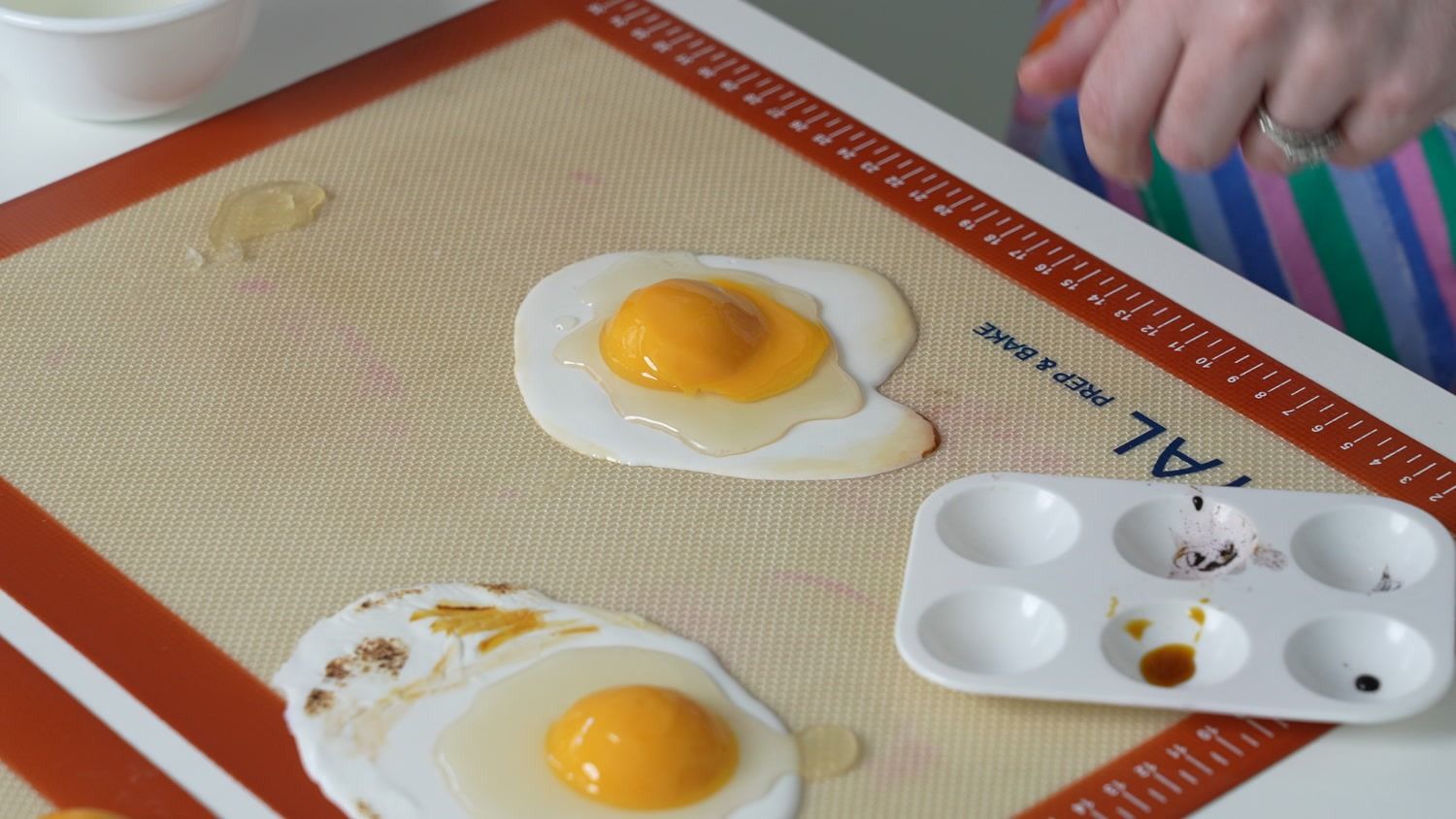 Hand-detailing a hyperrealistic fried egg made of cake on a baking mat
